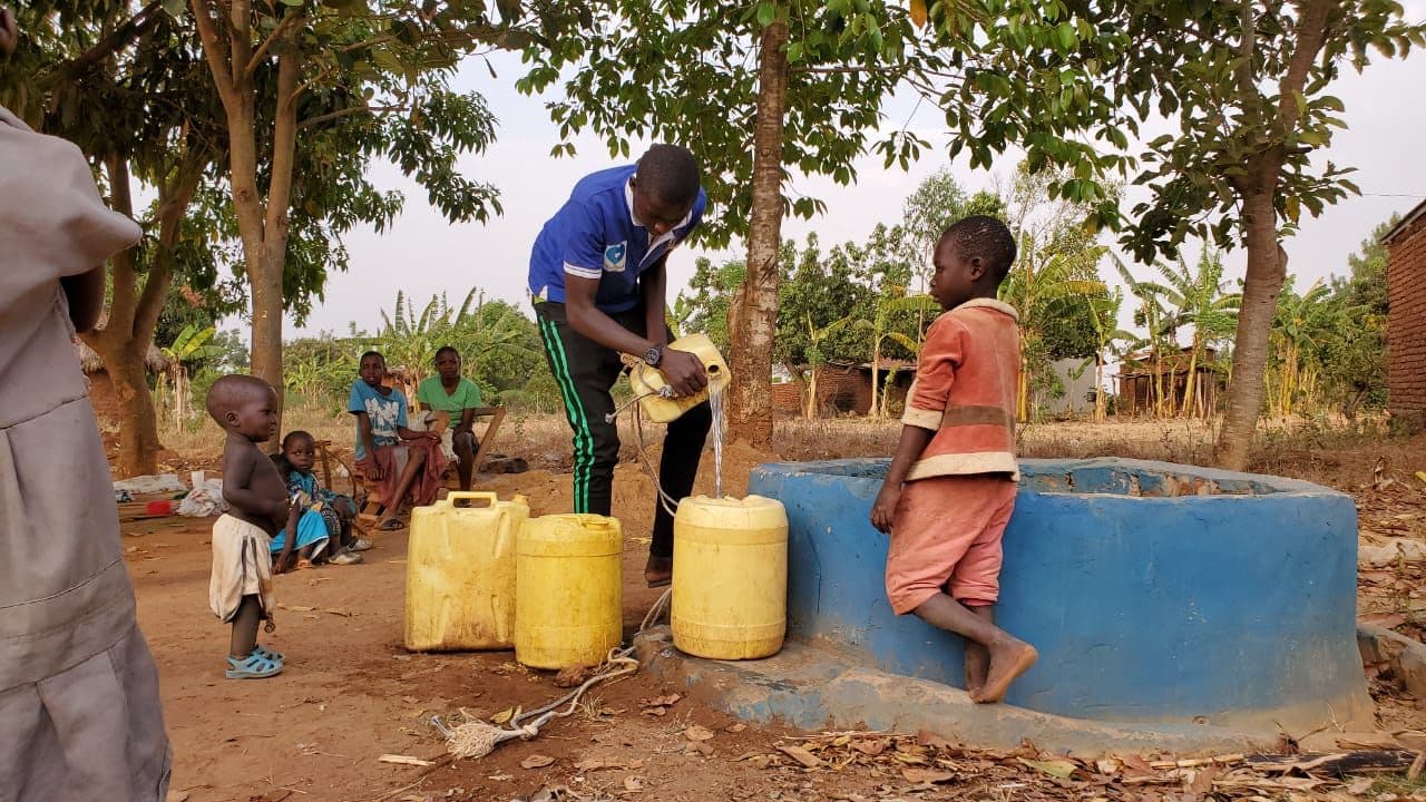 A volunteer filling a jerrycan beside a community well in Uganda
